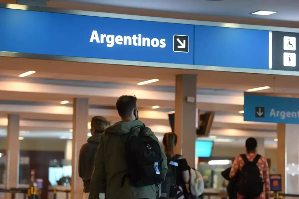 People walking in an airport under a blue sign indicating access for Argentinians People walking in an airport under a blue sign indicating access for Argentinians