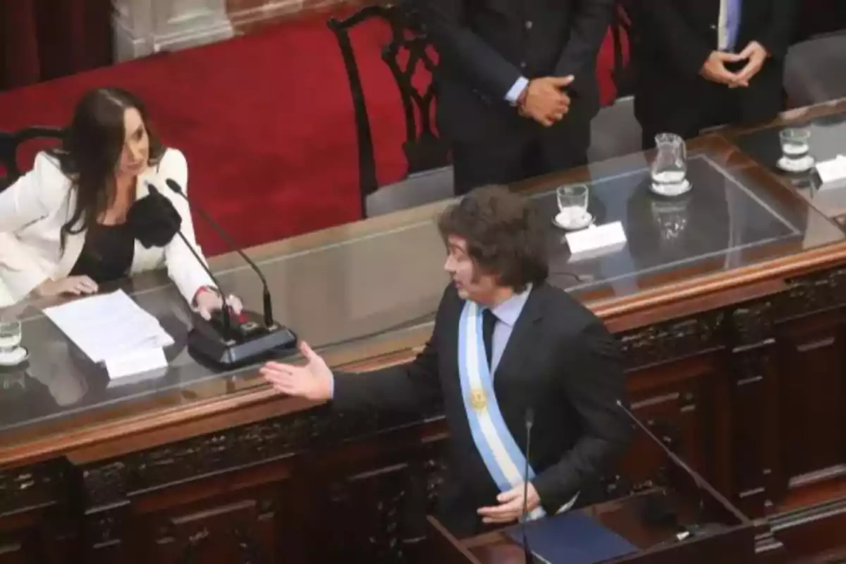 Una mujer con saco blanco y un hombre con banda presidencial conversan en un recinto parlamentario Una mujer con saco blanco y un hombre con banda presidencial conversan en un recinto parlamentario