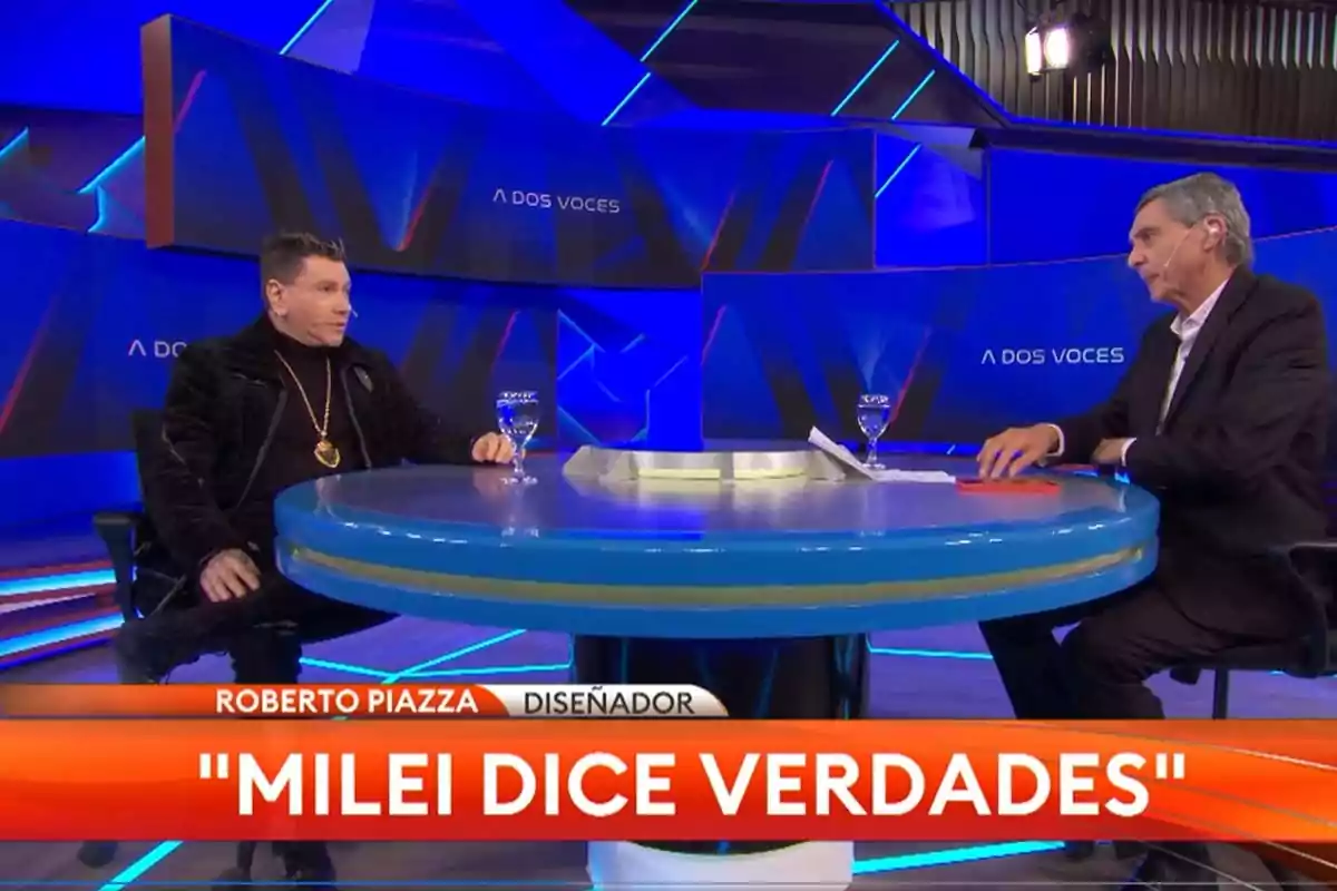 Dos personas sentadas en una mesa redonda durante una entrevista televisiva en un estudio con luces azules y el texto Milei dice verdades en la parte inferior de la pantalla Dos personas sentadas en una mesa redonda durante una entrevista televisiva en un estudio con luces azules y el texto Milei dice verdades en la parte inferior de la pantalla