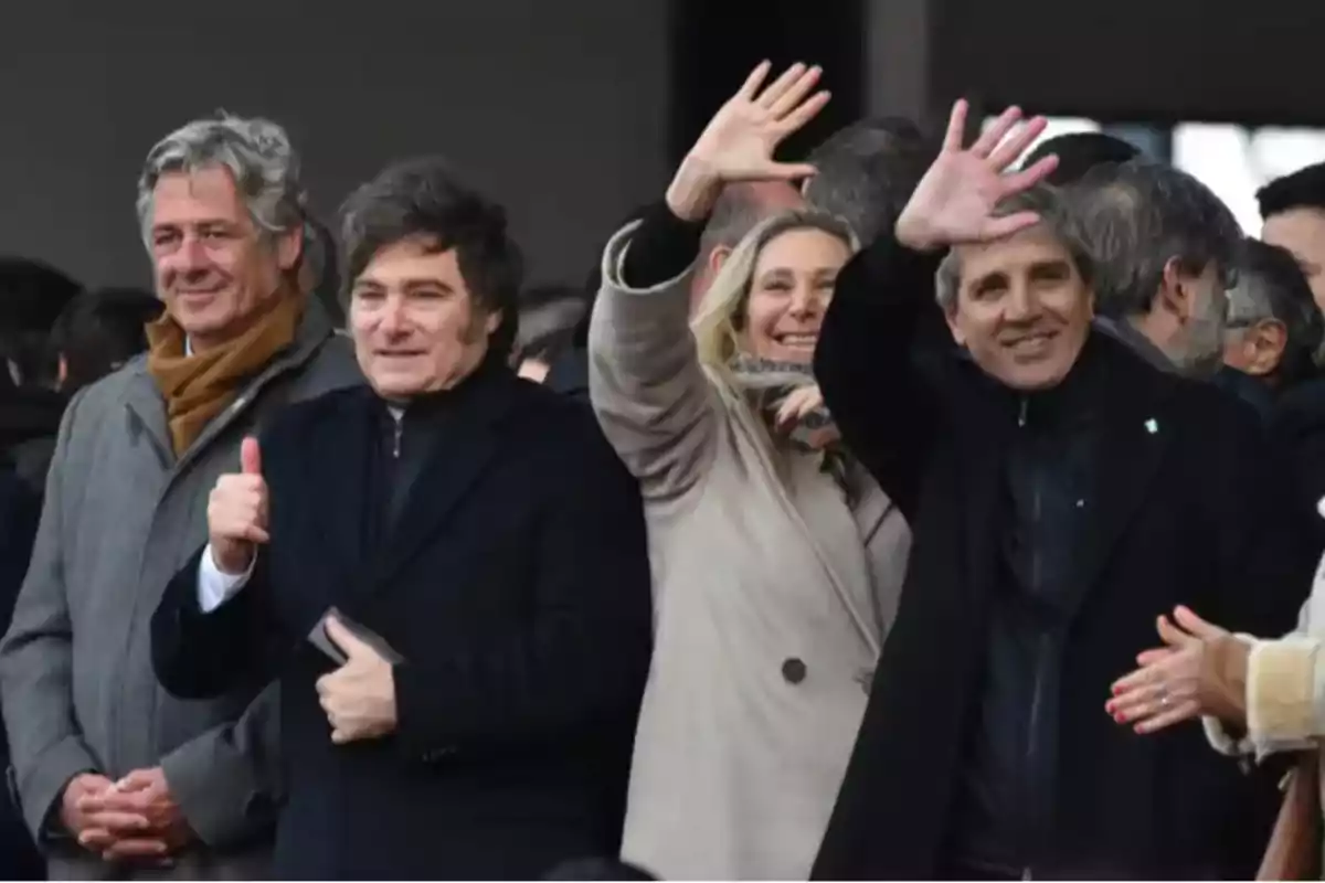 Grupo de personas abrigadas sonríen y saludan con la mano en alto en un evento al aire libre Grupo de personas abrigadas sonríen y saludan con la mano en alto en un evento al aire libre