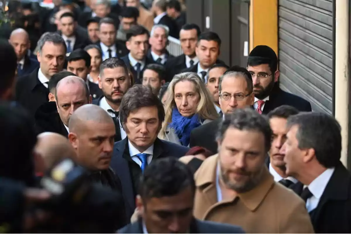 A group of people dressed formally walks down a street with serious and focused expressions.