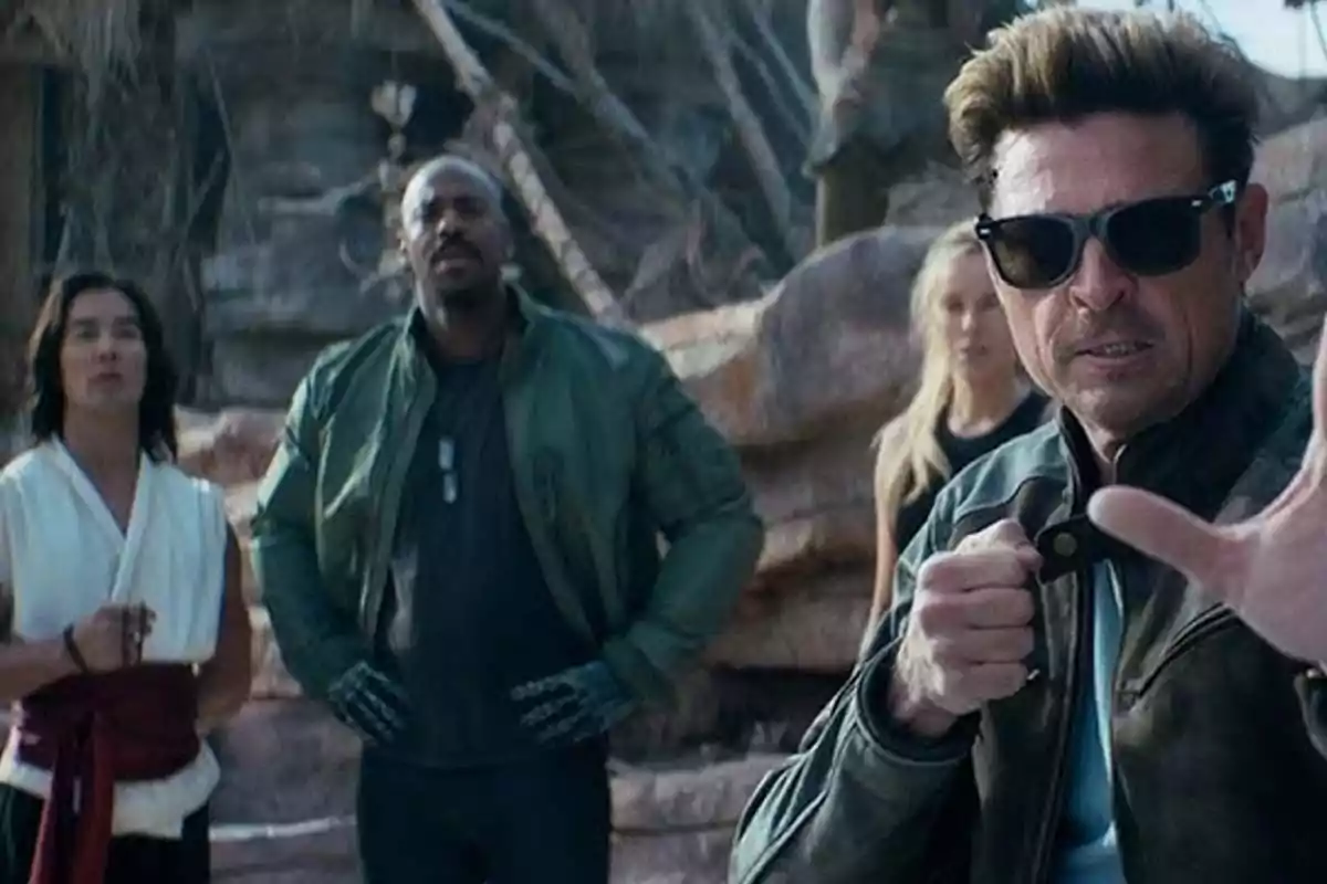Four people in varied clothing are outdoors in a rocky environment; one of them at the front is wearing sunglasses and appears to be in a defensive stance. Four people in varied clothing are outdoors in a rocky environment; one of them at the front is wearing sunglasses and appears to be in a defensive stance.