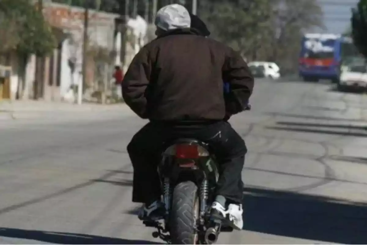 Two people are riding a motorcycle down an urban street during the day.