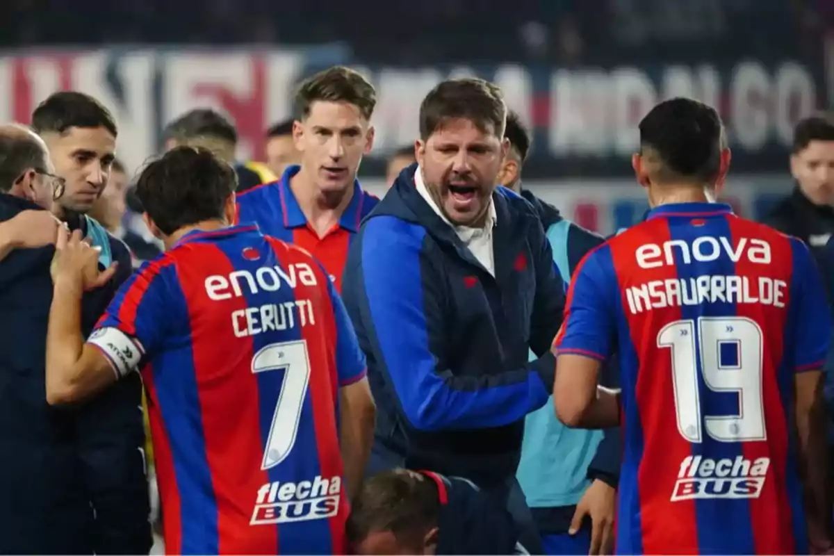 Entrenador y jugadores de un equipo de fútbol con camisetas rojas y azules celebran y se comunican en el campo durante un partido Entrenador y jugadores de un equipo de fútbol con camisetas rojas y azules celebran y se comunican en el campo durante un partido