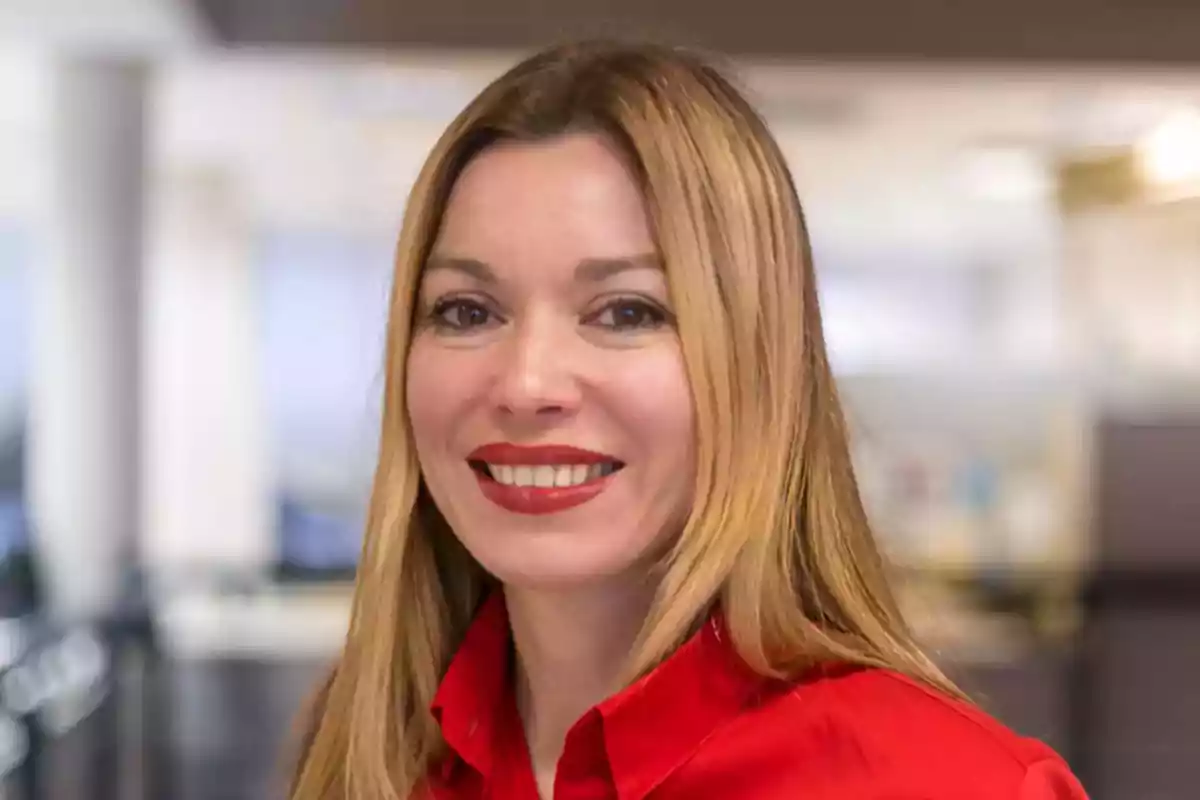 Mujer de cabello rubio y lacio con camisa roja sonriendo en un entorno de oficina desenfocado