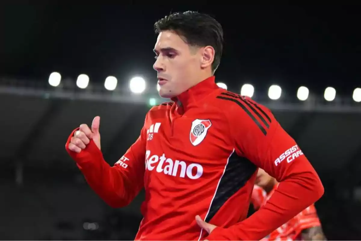 Soccer player in a red River Plate uniform in a lit stadium giving a thumbs-up gesture Soccer player in a red River Plate uniform in a lit stadium giving a thumbs-up gesture