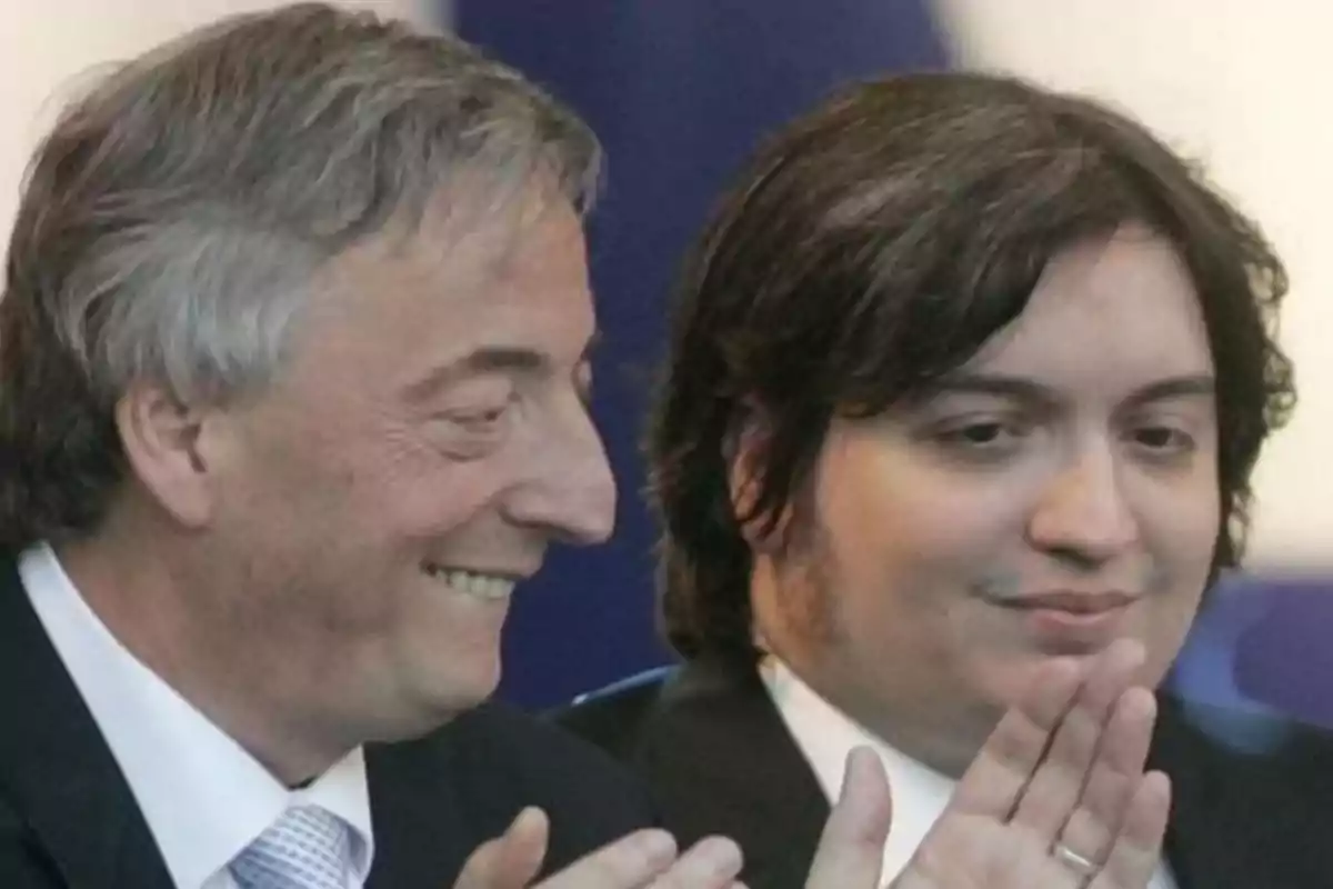 Two men in suits smile and applaud at an event. Two men in suits smile and applaud at an event.