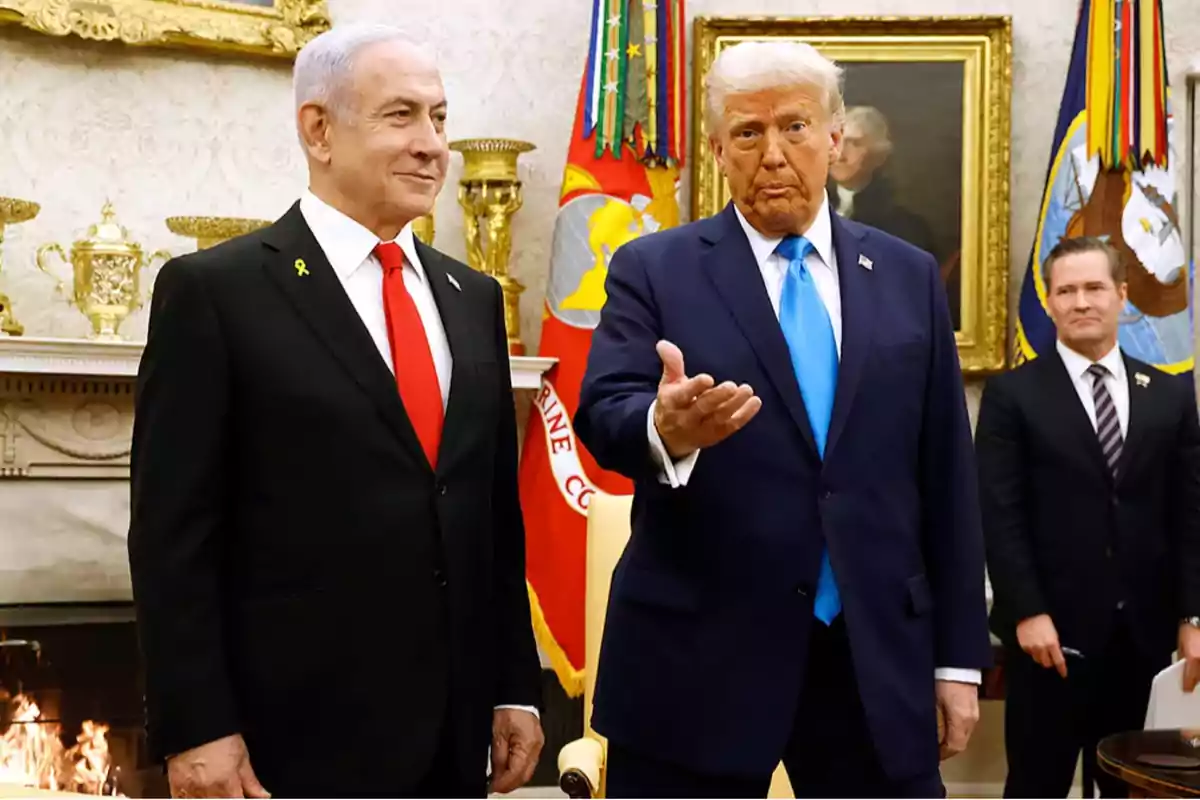 Two men in suits pose in an elegant room with flags and golden decorations in the background while a third man watches from the right.