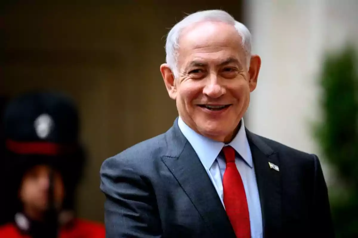 Gray-haired man in a dark suit and red tie smiling in a formal setting