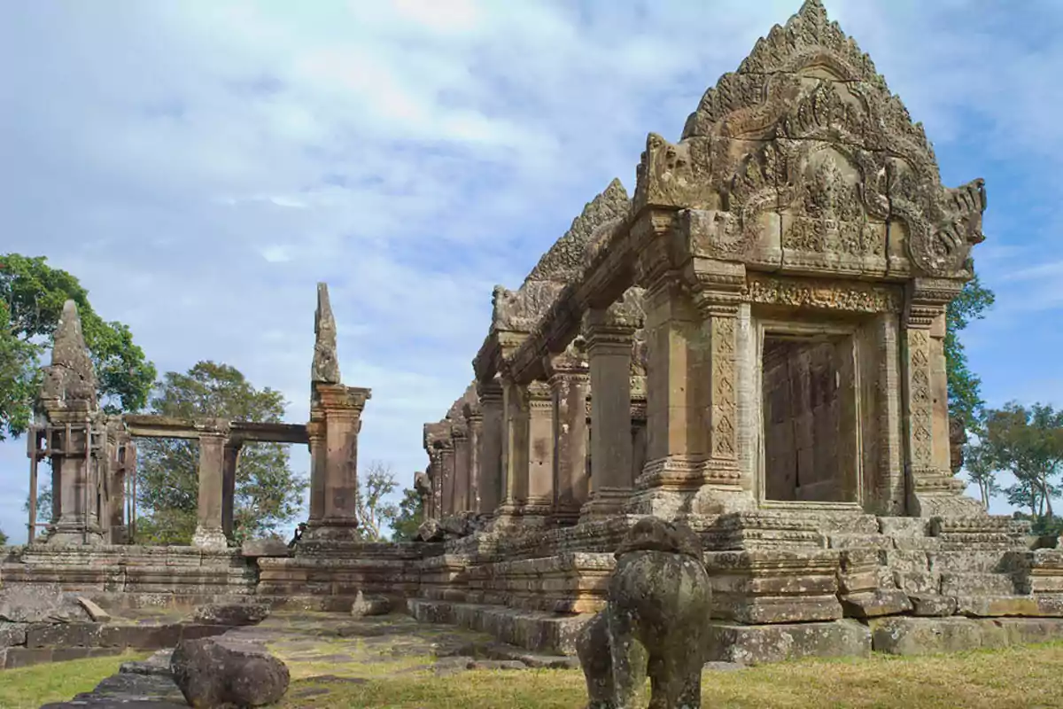 Ancient stone temple with carved details and columns, surrounded by vegetation under a partly cloudy sky Ancient stone temple with carved details and columns, surrounded by vegetation under a partly cloudy sky