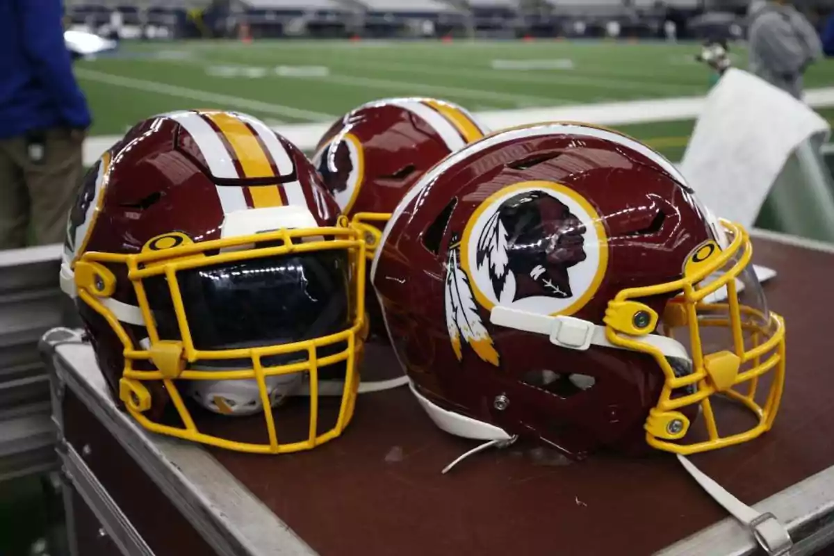 Tres cascos de fútbol americano del equipo Washington Redskins sobre una mesa en un estadio Tres cascos de fútbol americano del equipo Washington Redskins sobre una mesa en un estadio