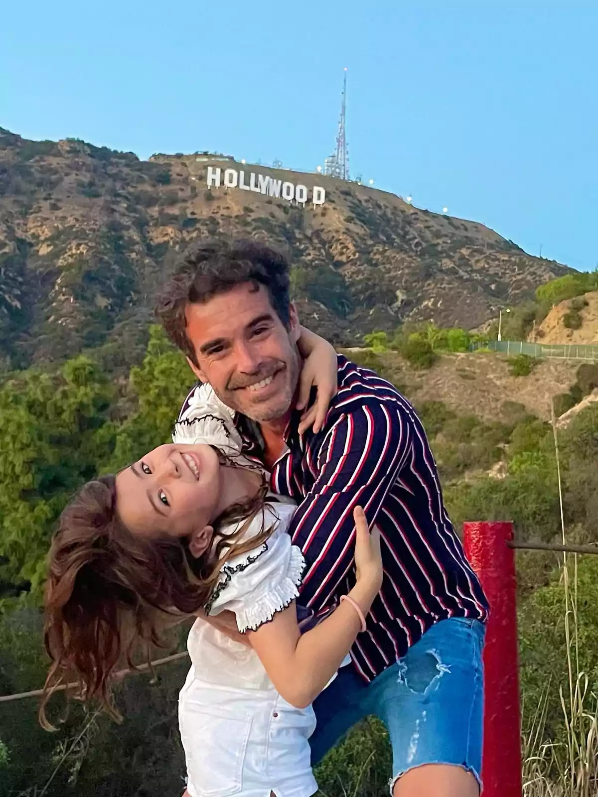 Man and girl smile hugging in front of the famous Hollywood sign on a hill. Man and girl smile hugging in front of the famous Hollywood sign on a hill.