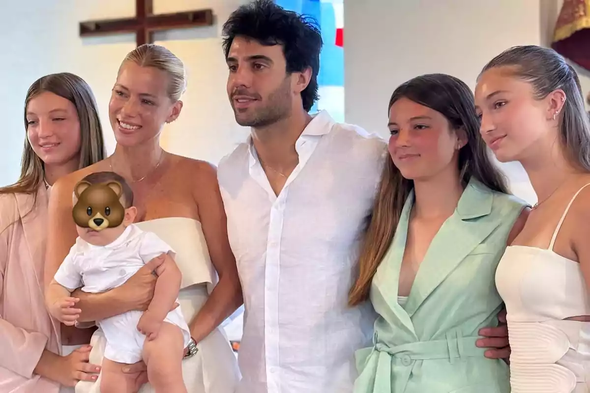Familia posando junta en un evento especial con un bebé en brazos y un emoji de oso cubriendo su rostro Familia posando junta en un evento especial con un bebé en brazos y un emoji de oso cubriendo su rostro