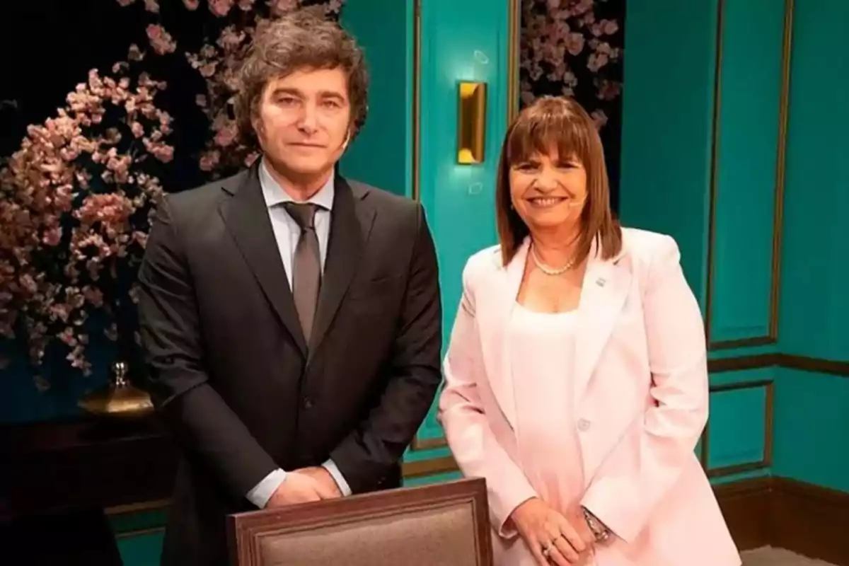 Dos personas posan sonrientes en un estudio decorado con flores y paredes turquesa Dos personas posan sonrientes en un estudio decorado con flores y paredes turquesa