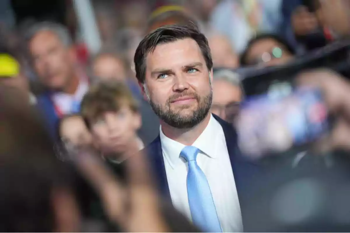 Bearded man in a suit with a light blue tie surrounded by people at a public event Bearded man in a suit with a light blue tie surrounded by people at a public event