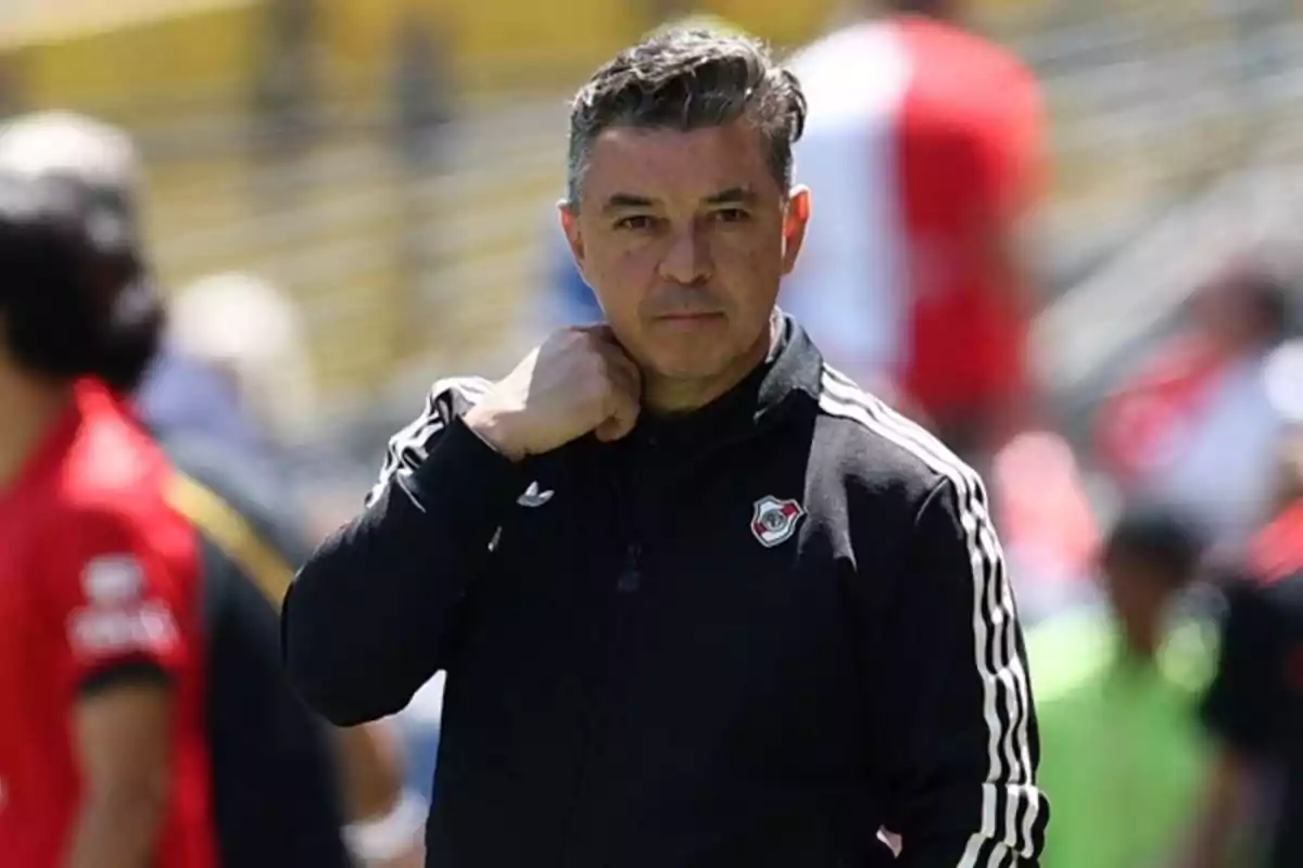 Entrenador de fútbol con chaqueta negra de River Plate en un estadio durante el día