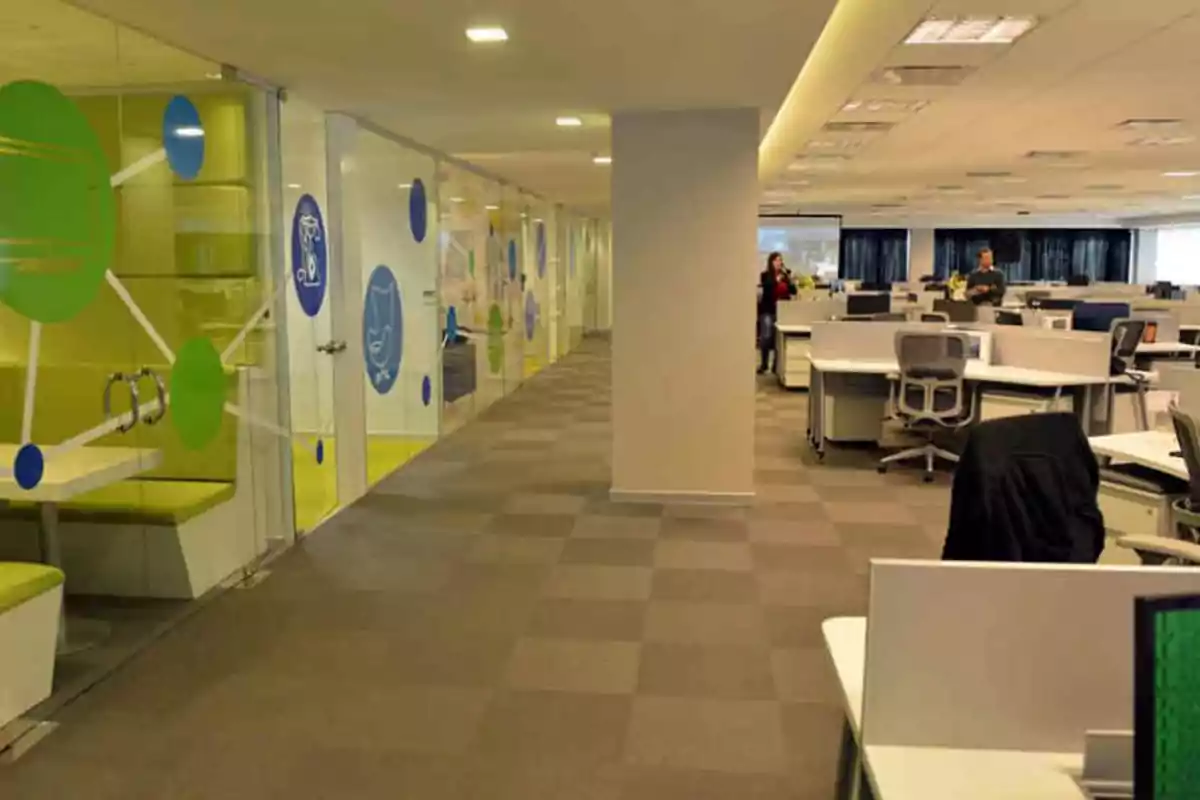 Modern office with white desks, ergonomic chairs, meeting booths with decorated glass walls, and a few people working in the background Modern office with white desks, ergonomic chairs, meeting booths with decorated glass walls, and a few people working in the background