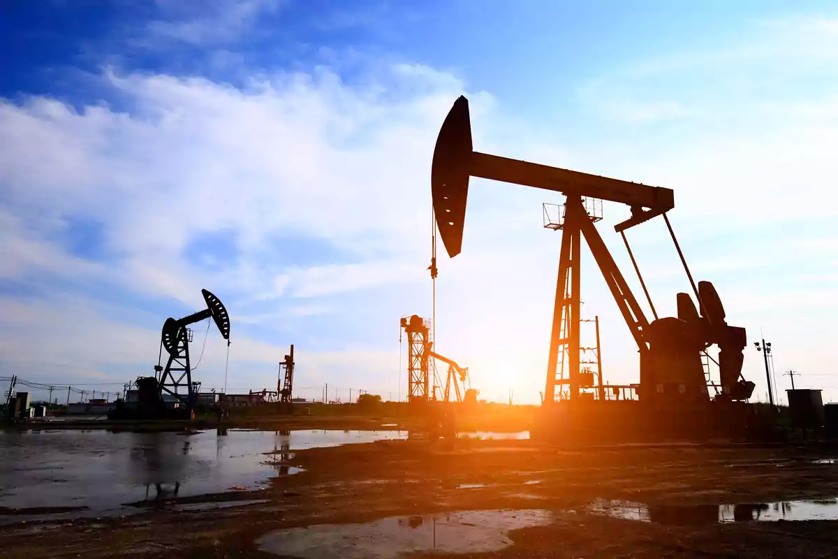 Maquinaria extractora de petróleo trabajando al atardecer en un campo petrolero Maquinaria extractora de petróleo trabajando al atardecer en un campo petrolero