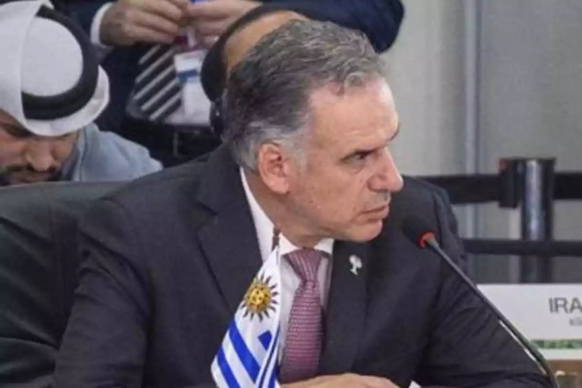 Hombre de traje sentado en una conferencia con una bandera de Uruguay frente a él