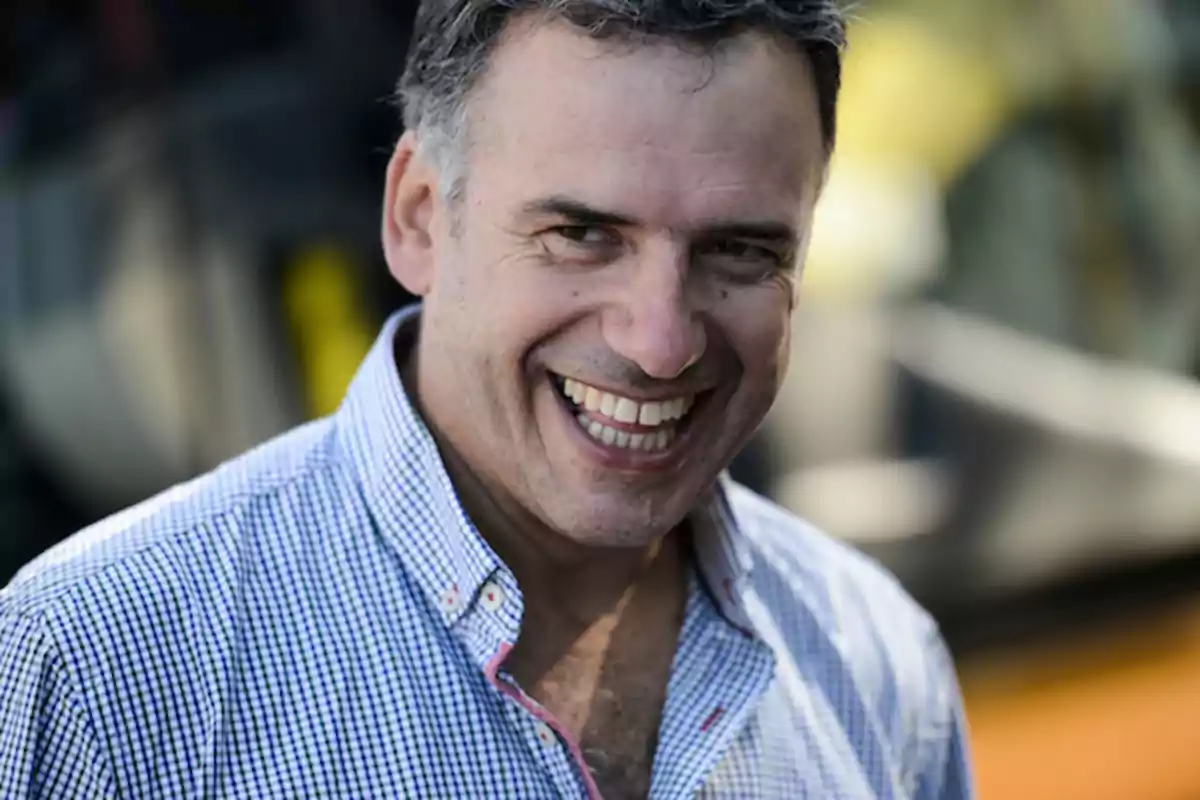 Middle-aged man smiling in a plaid jersey in a blurred outdoor setting
