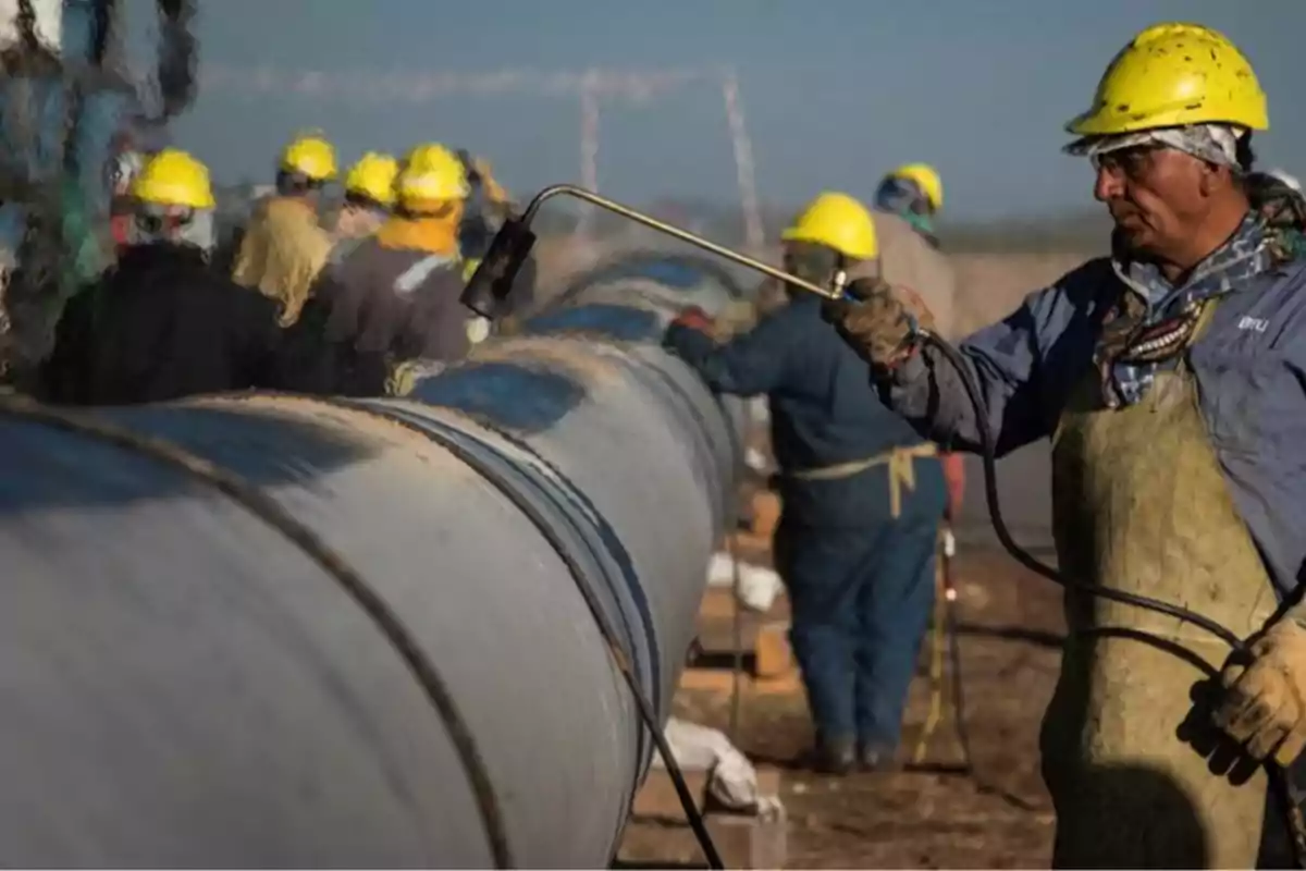Trabajadores con casco amarillo y equipo de protección aplican calor a una tubería grande en una obra al aire libre