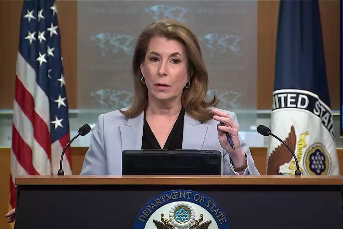 Mujer hablando en una conferencia de prensa oficial del Departamento de Estado de Estados Unidos con banderas y un podio al frente. Mujer hablando en una conferencia de prensa oficial del Departamento de Estado de Estados Unidos con banderas y un podio al frente.