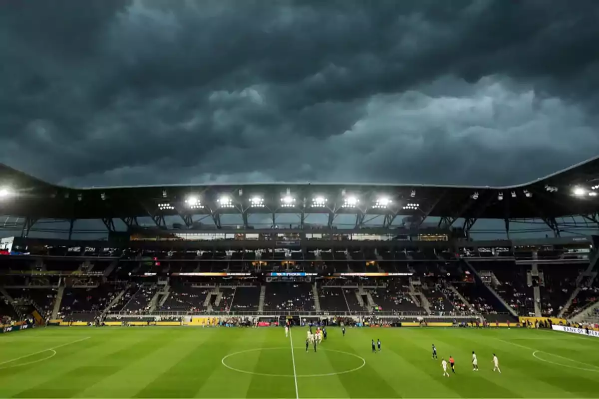 Estadio de fútbol iluminado con cielo nublado y jugadores en el campo Estadio de fútbol iluminado con cielo nublado y jugadores en el campo