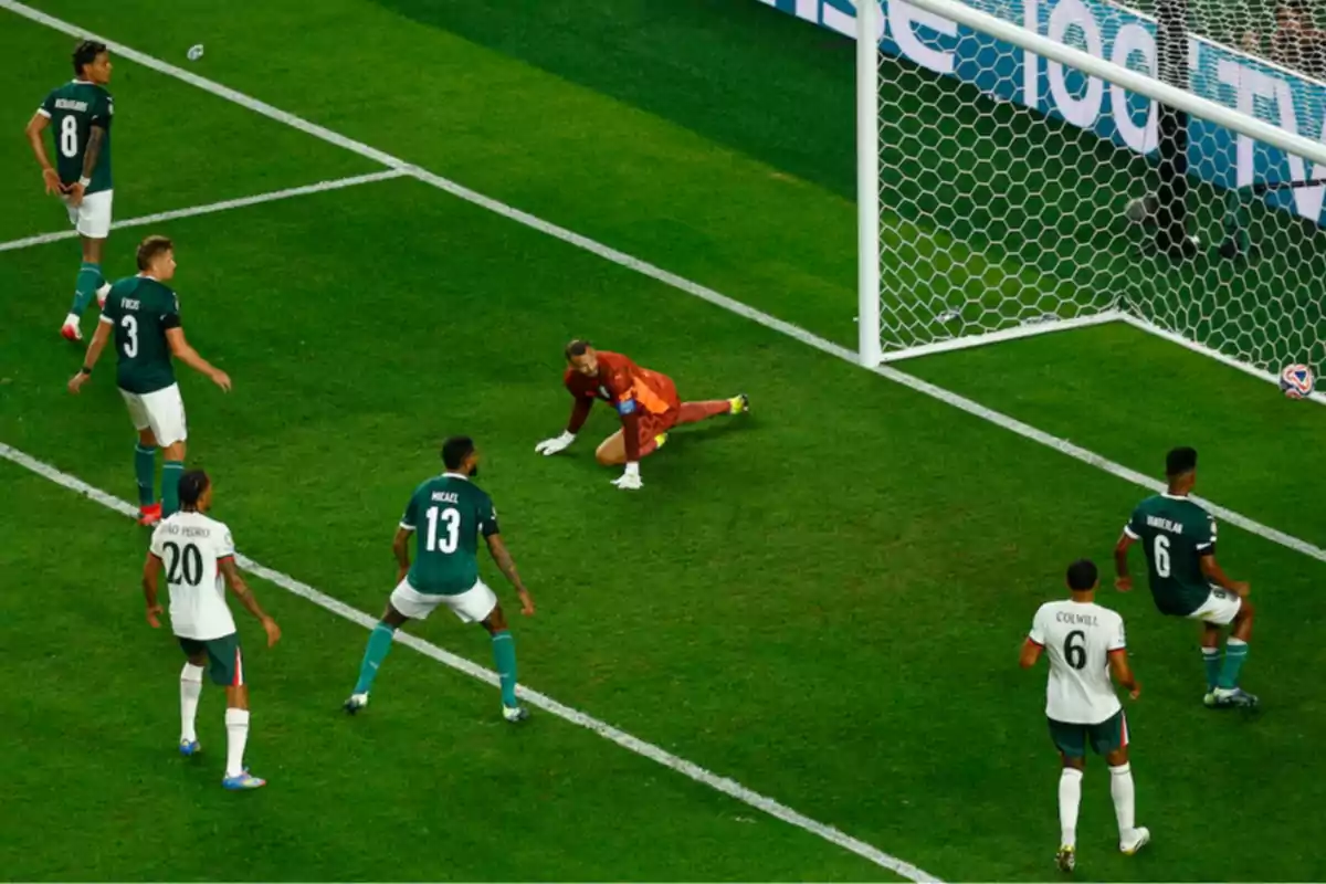 Soccer players watch the ball inside the goal while the goalkeeper is on the ground after a play during a match. Soccer players watch the ball inside the goal while the goalkeeper is on the ground after a play during a match.