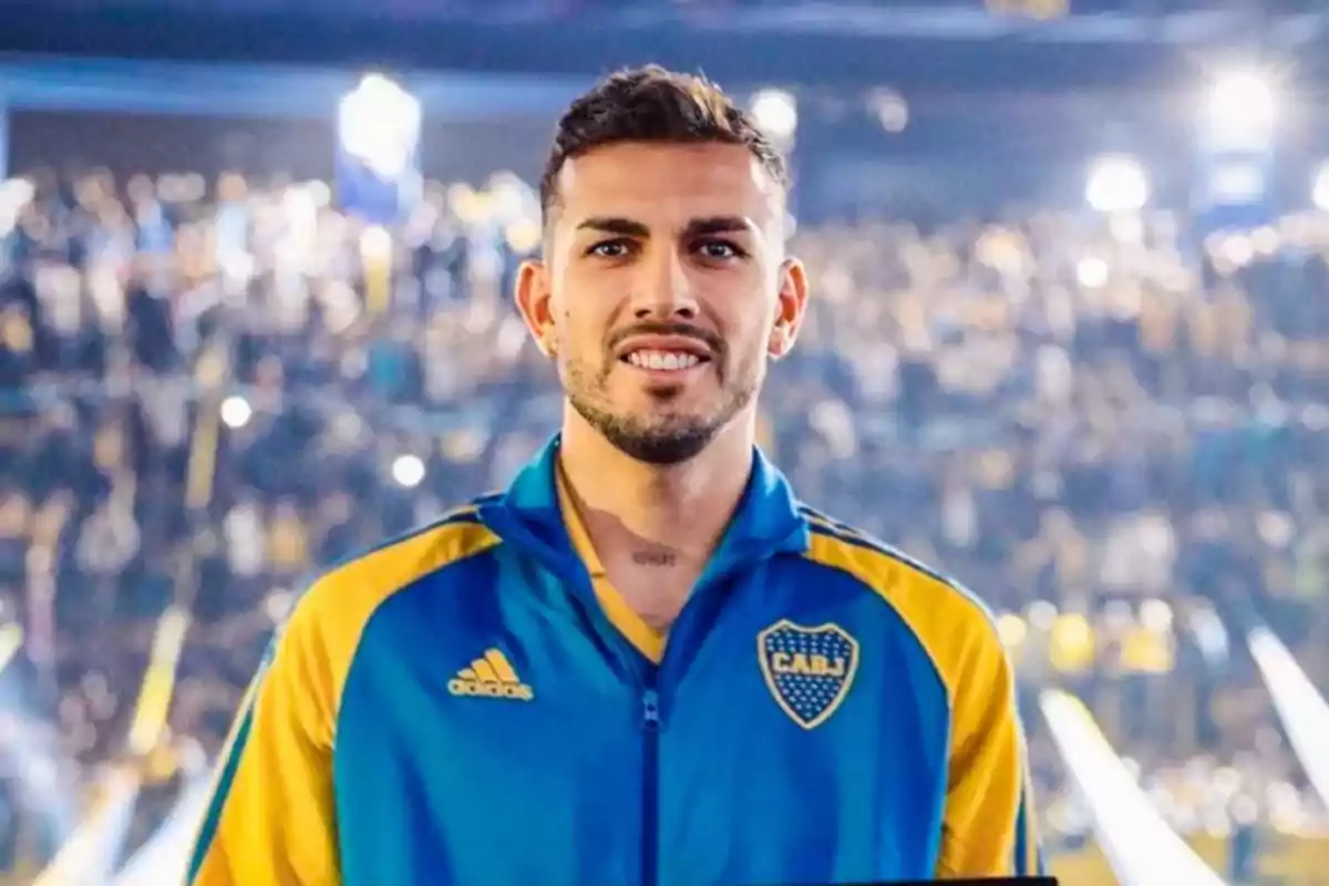 Soccer player wearing a blue and yellow Boca Juniors jacket smiling in front of a crowd in a lit-up stadium