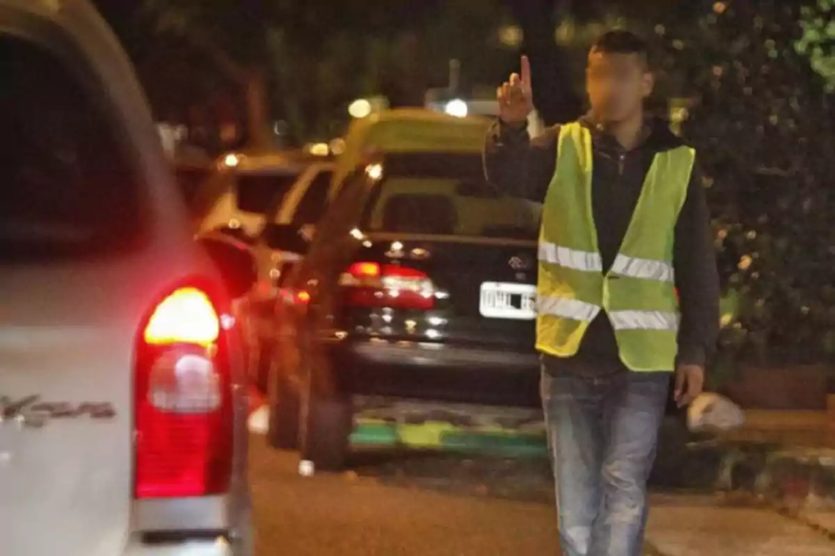 Hombre con chaleco reflejante señalando con el dedo mientras dirige el estacionamiento de autos en la calle por la noche Hombre con chaleco reflejante señalando con el dedo mientras dirige el estacionamiento de autos en la calle por la noche