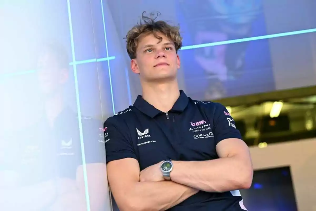 Young man wearing an Alpine Formula 1 team jersey posing with his arms crossed and his reflection on a glass wall Young man wearing an Alpine Formula 1 team jersey posing with his arms crossed and his reflection on a glass wall