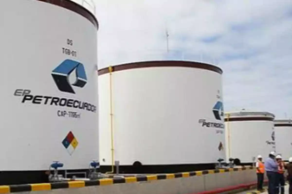 Varios tanques de almacenamiento de la empresa Petroecuador con personas usando cascos y chalecos de seguridad en primer plano