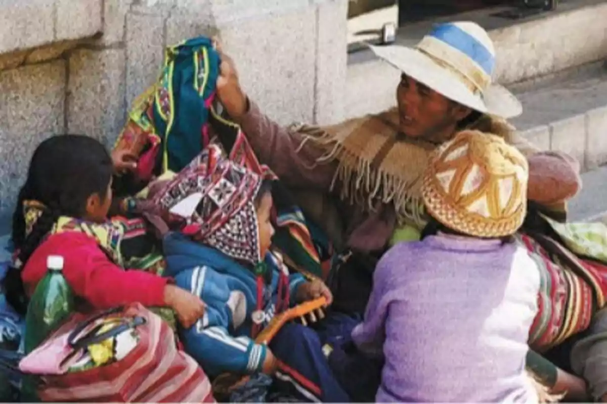 Familia sentada en la calle con ropa tradicional andina y gorros coloridos conversando y rodeada de bolsas y mantas Familia sentada en la calle con ropa tradicional andina y gorros coloridos conversando y rodeada de bolsas y mantas