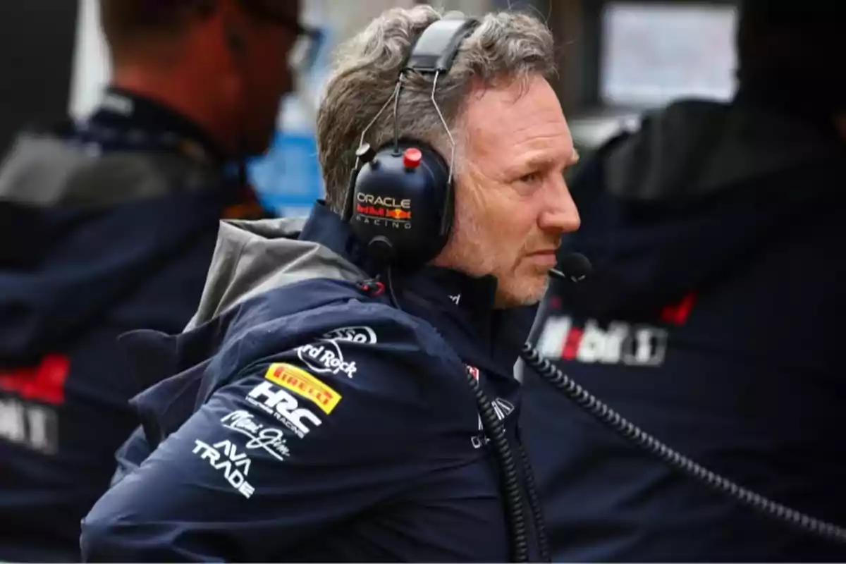 Hombre con auriculares y micrófono vistiendo chaqueta de equipo de automovilismo en un entorno de competencia