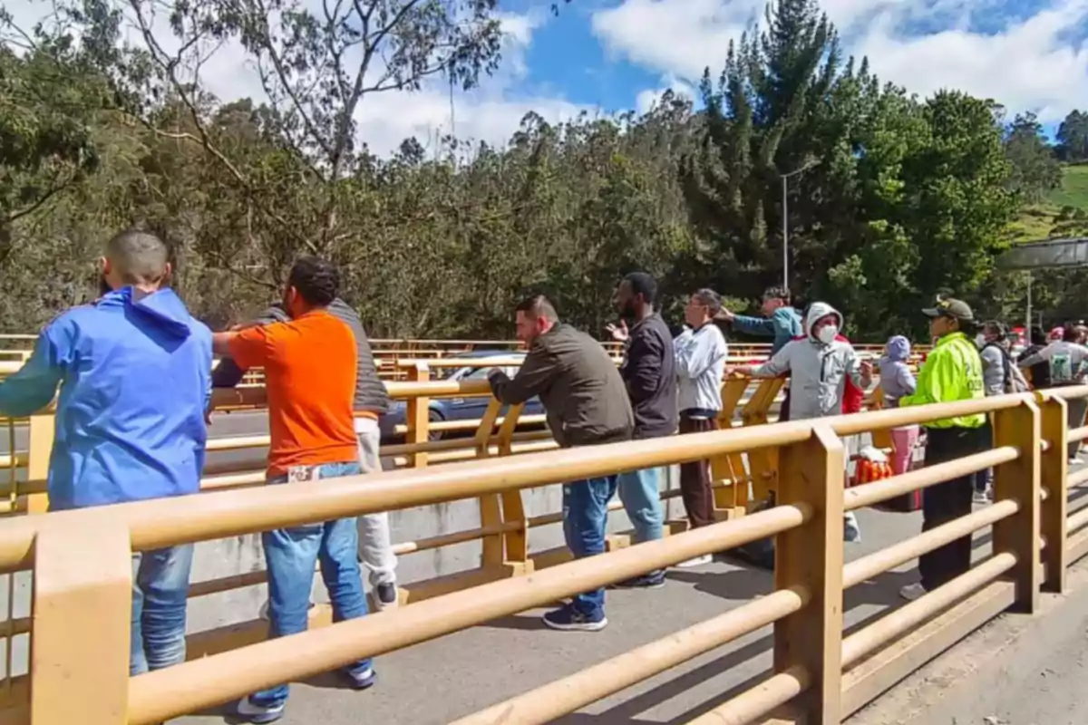 Varias personas están de pie junto a una baranda amarilla en un puente al aire libre rodeado de árboles y cielo azul Varias personas están de pie junto a una baranda amarilla en un puente al aire libre rodeado de árboles y cielo azul