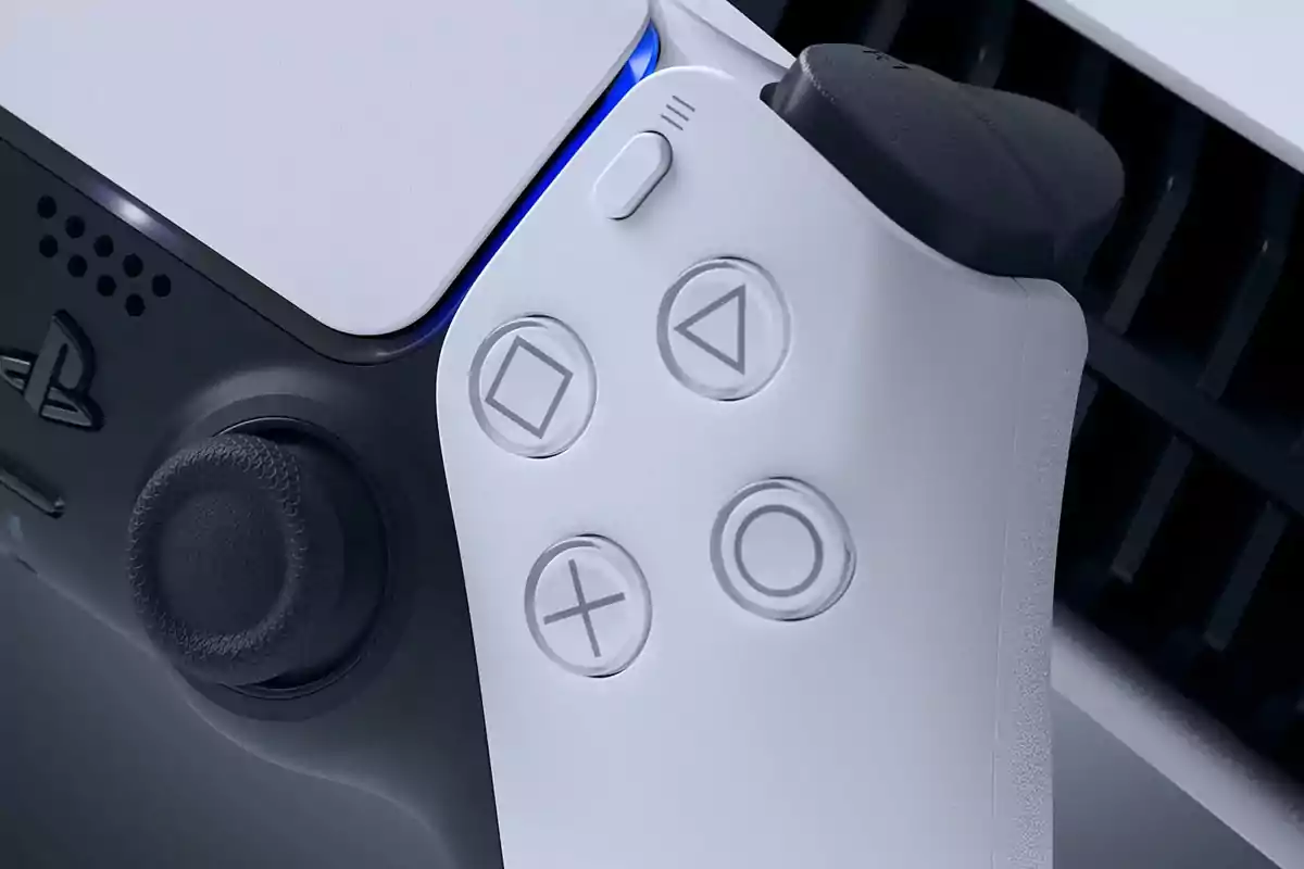 Control de videojuego blanco y negro de PlayStation 5 en primer plano mostrando los botones característicos y parte de la consola al fondo Control de videojuego blanco y negro de PlayStation 5 en primer plano mostrando los botones característicos y parte de la consola al fondo
