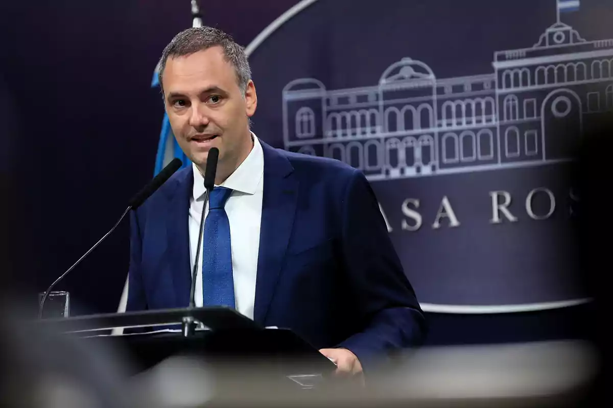 Hombre de traje azul hablando en una conferencia de prensa con fondo institucional de la Casa Rosada