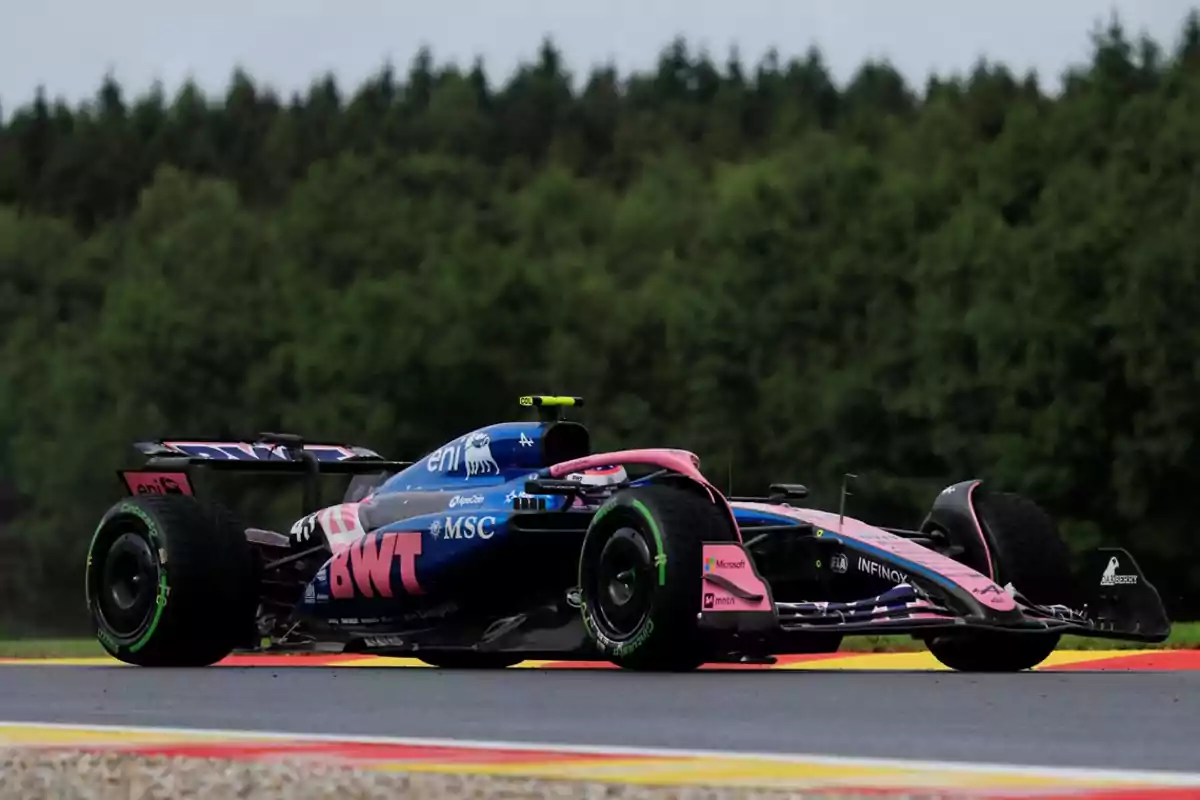 Auto de Fórmula 1 de color azul y rosa circulando en una pista con fondo de árboles Auto de Fórmula 1 de color azul y rosa circulando en una pista con fondo de árboles