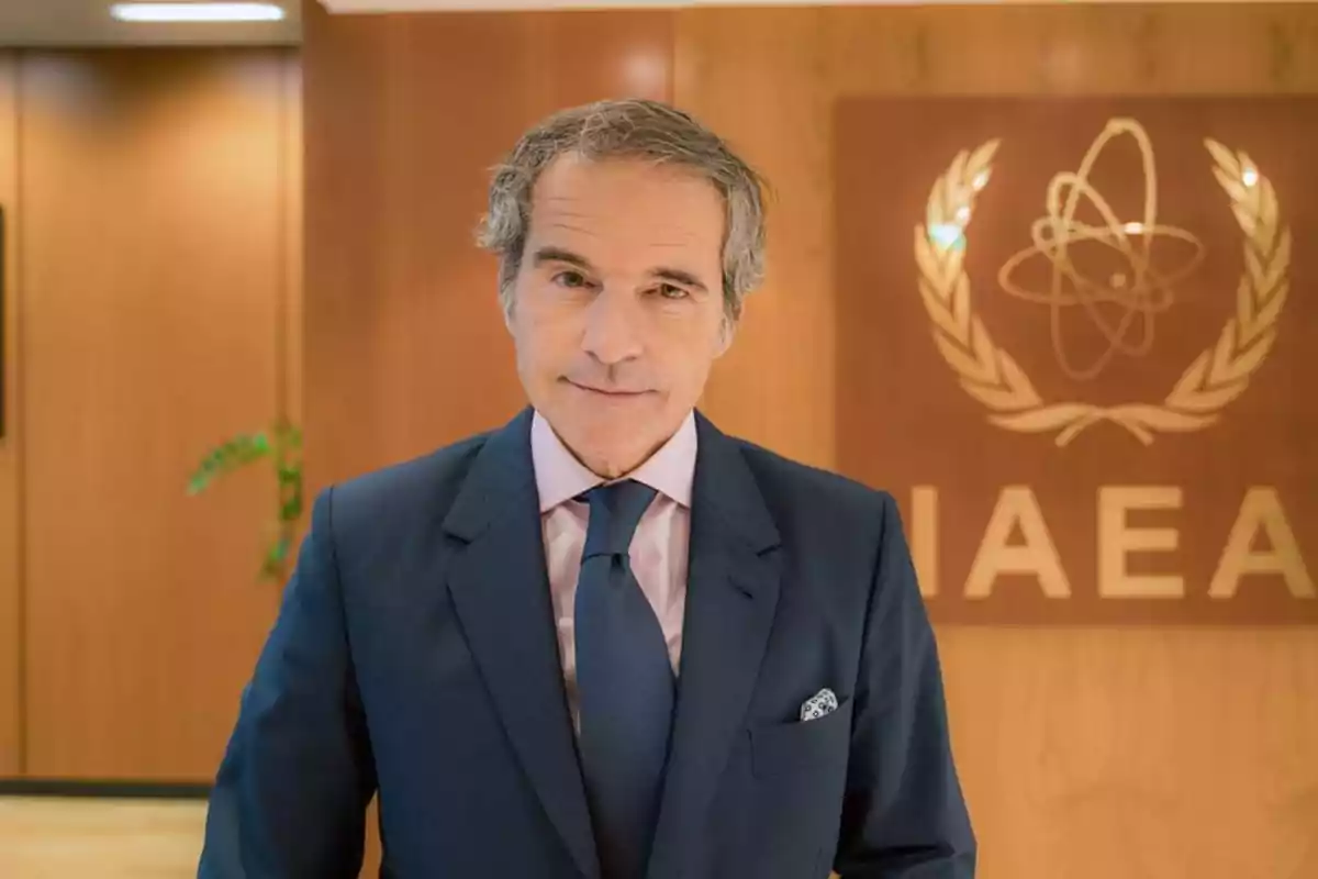 Hombre de cabello canoso con traje azul y corbata posando frente a un fondo de madera con el logotipo y las siglas de la IAEA Hombre de cabello canoso con traje azul y corbata posando frente a un fondo de madera con el logotipo y las siglas de la IAEA