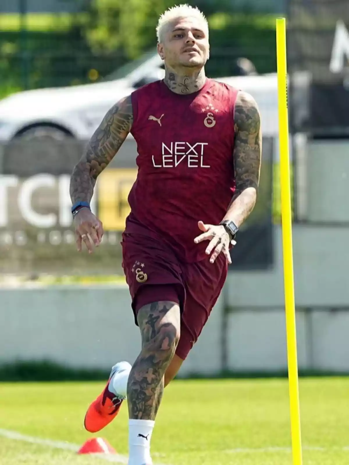 Futbolista con cabello rubio platinado y tatuajes entrenando en un campo de fútbol con uniforme burdeos del Galatasaray Futbolista con cabello rubio platinado y tatuajes entrenando en un campo de fútbol con uniforme burdeos del Galatasaray