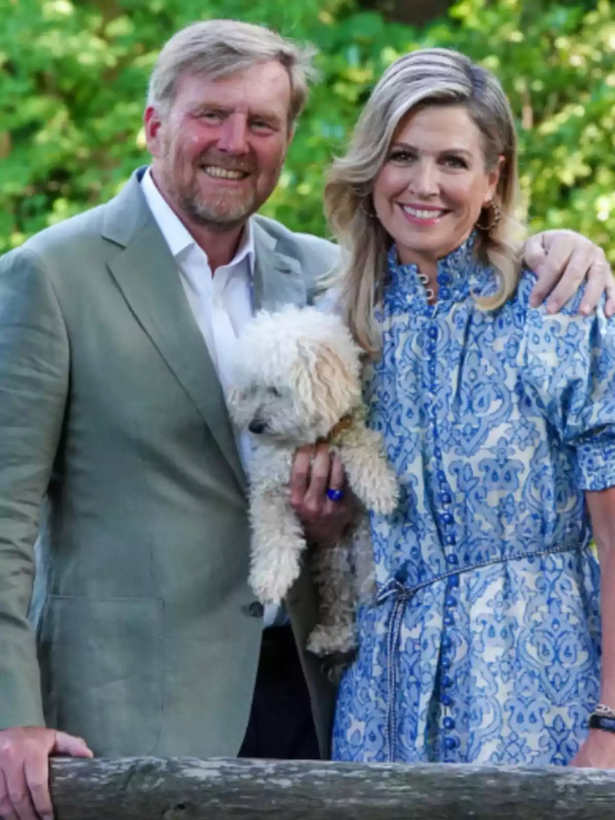 Smiling couple posing outdoors with a small curly-haired dog in their arms, surrounded by green vegetation Smiling couple posing outdoors with a small curly-haired dog in their arms, surrounded by green vegetation