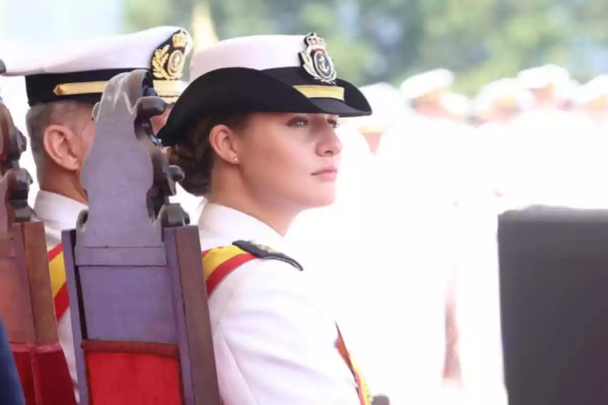 Young woman in a white naval uniform and officer’s cap sitting on a wooden chair during an official ceremony Young woman in a white naval uniform and officer’s cap sitting on a wooden chair during an official ceremony