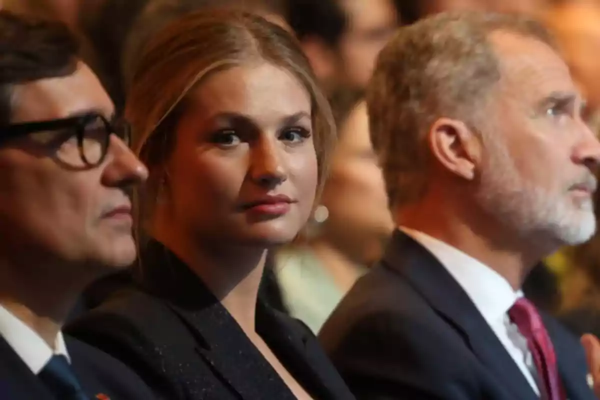 Tres personas sentadas en un evento formal con la mujer en el centro mirando hacia la cámara Tres personas sentadas en un evento formal con la mujer en el centro mirando hacia la cámara