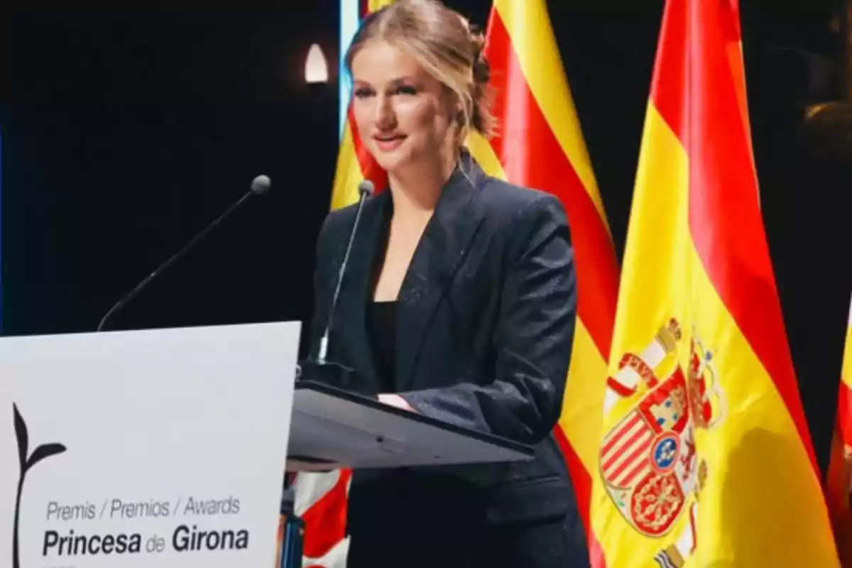 Mujer joven de cabello recogido hablando en un podio durante una ceremonia de premios con banderas de España al fondo