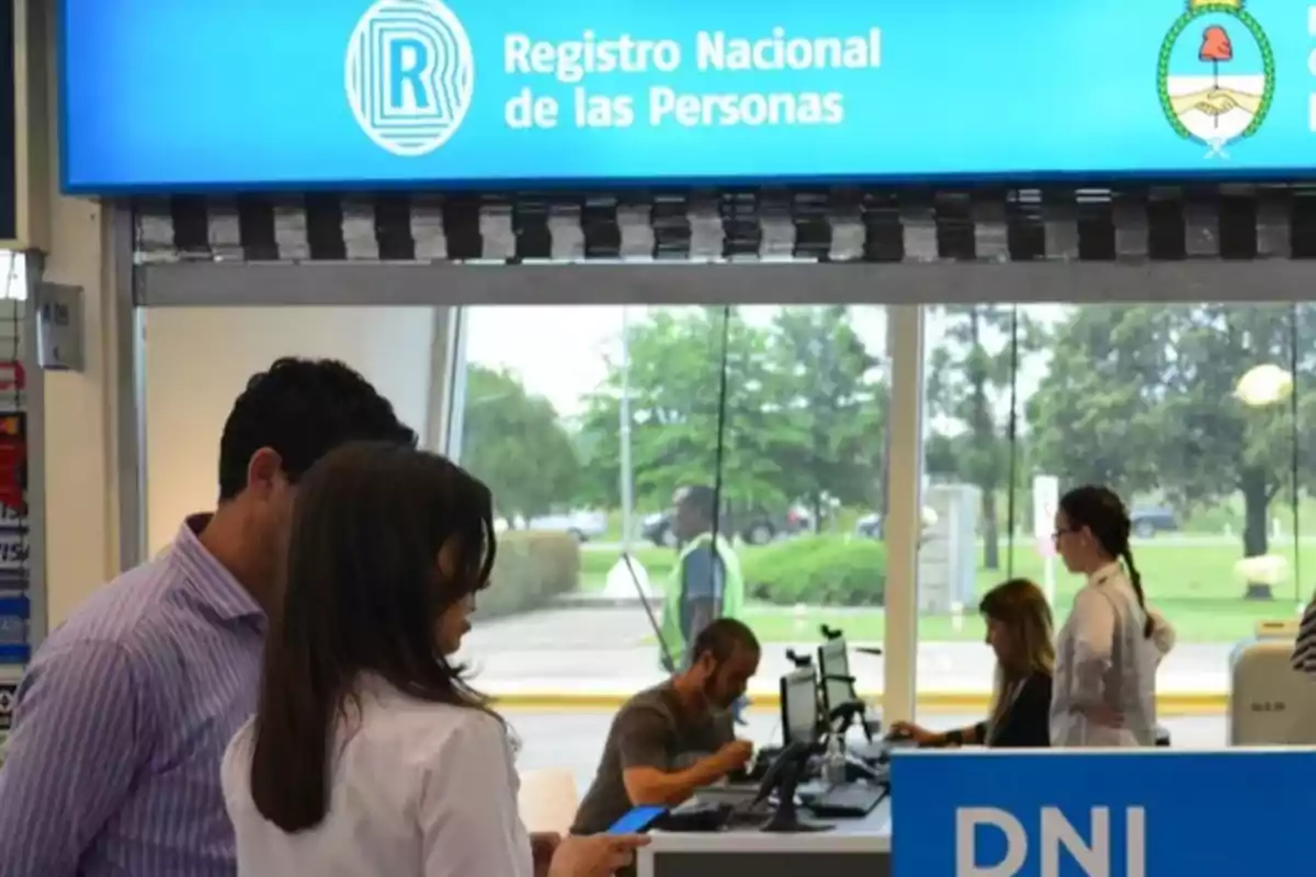 People carrying out procedures at a National Registry of Persons office with blue signs and computers on the counter People carrying out procedures at a National Registry of Persons office with blue signs and computers on the counter