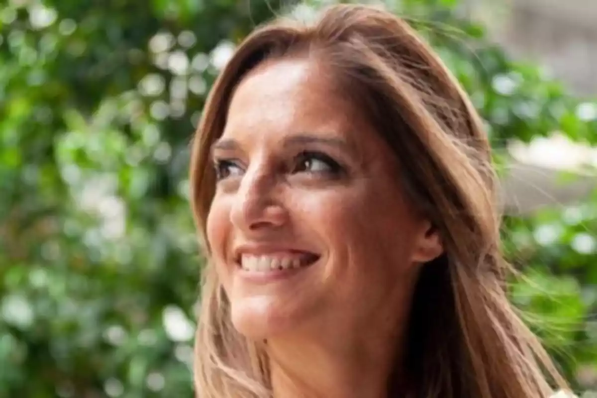 Smiling light brown-haired woman looking to the side with a blurred vegetation background
