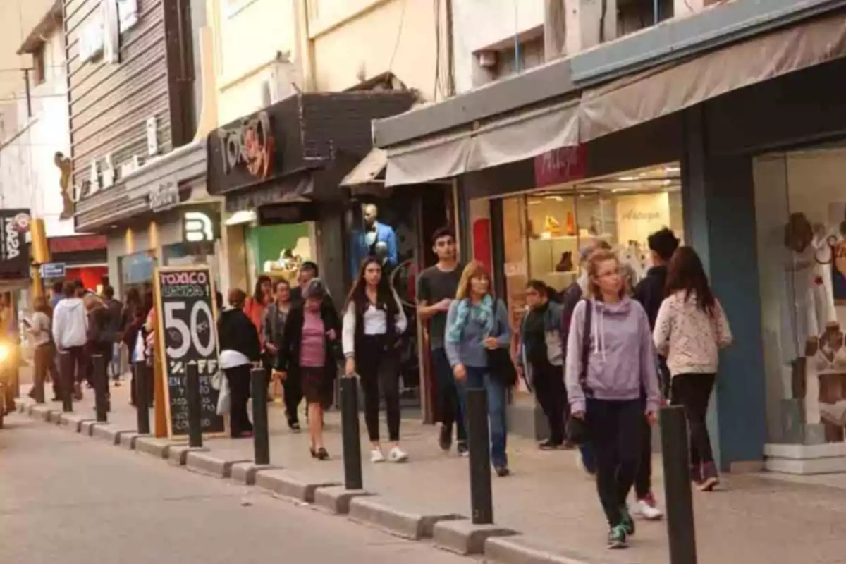 People walking down a shopping street with stores and a discount sign