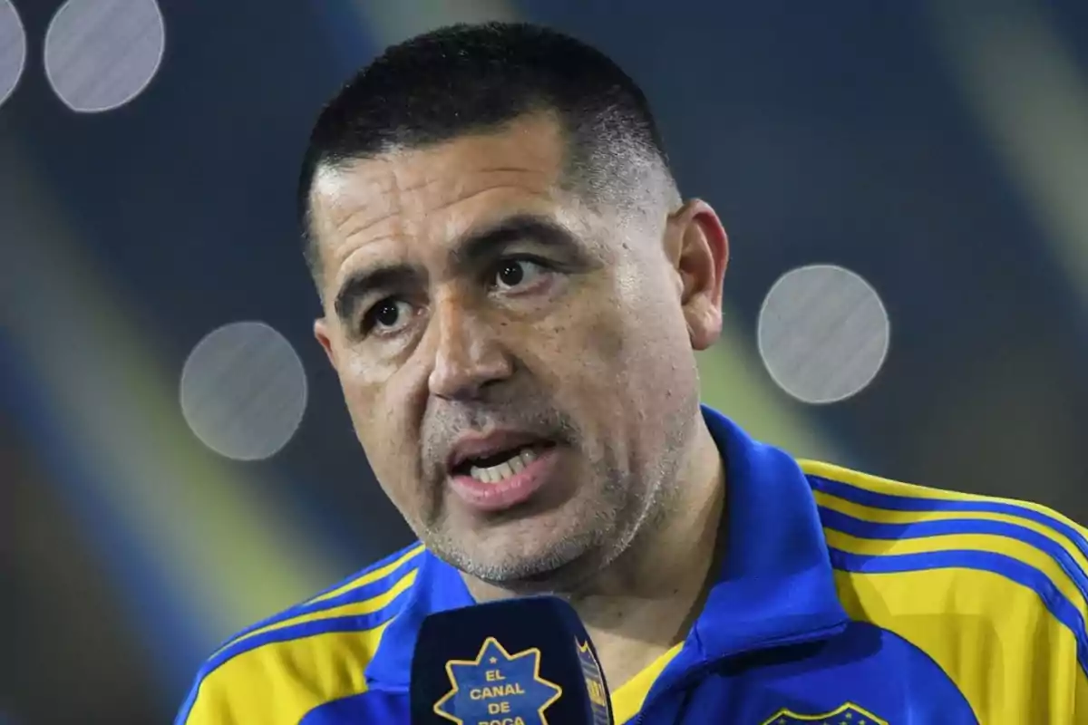 Hombre con camiseta azul y amarilla hablando frente a un micrófono en un estadio Hombre con camiseta azul y amarilla hablando frente a un micrófono en un estadio