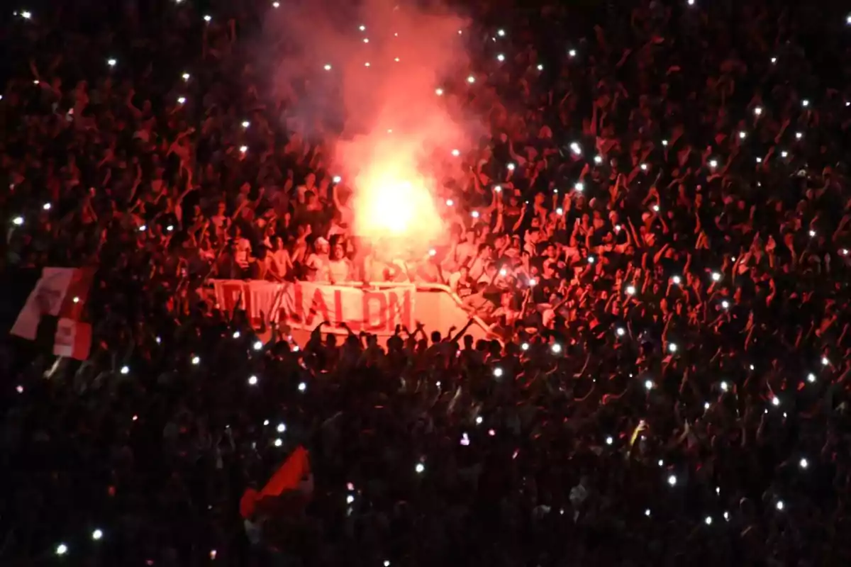 Fans in a stadium celebrate with flares and cell phone lights during a sporting event. Fans in a stadium celebrate with flares and cell phone lights during a sporting event.