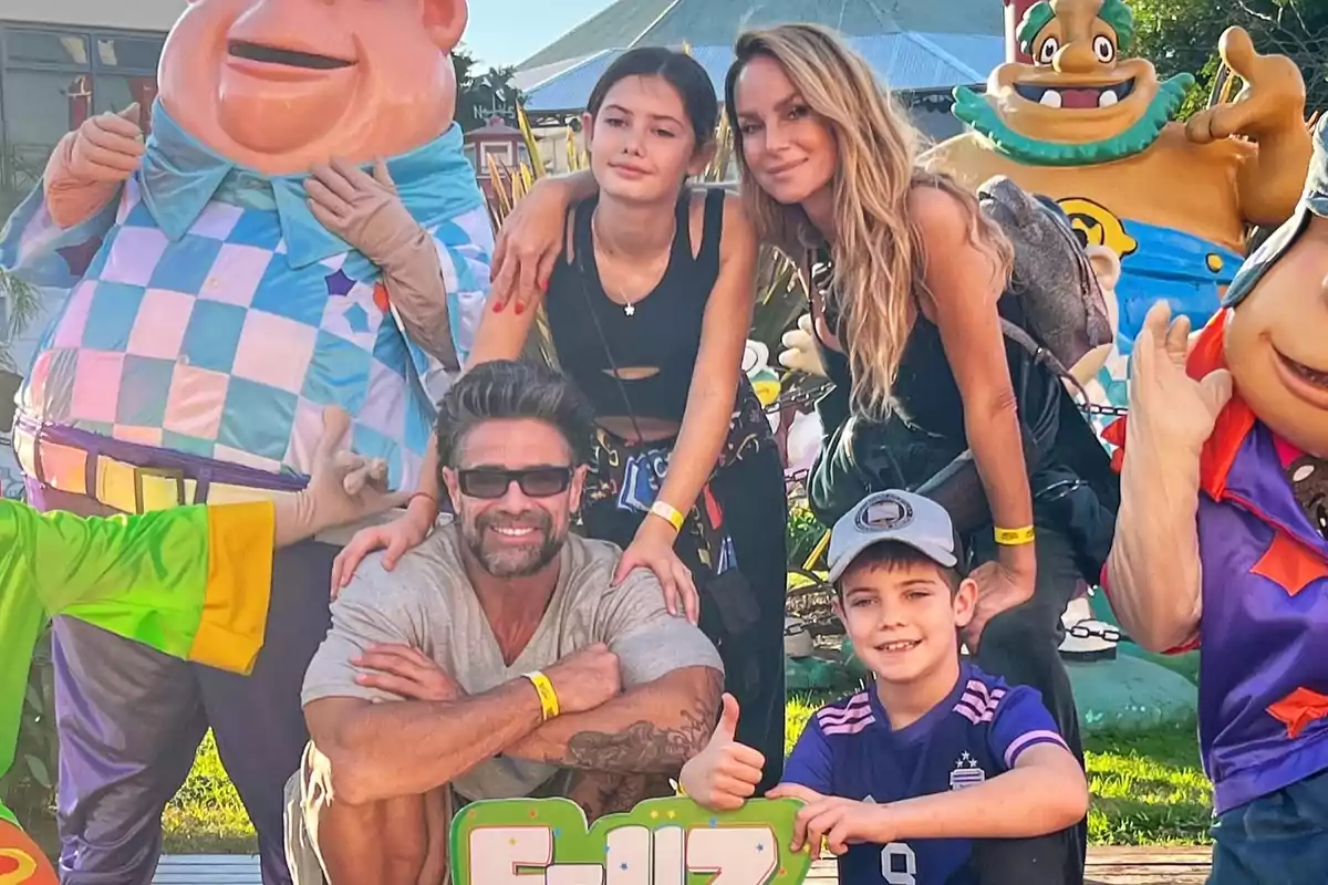 A smiling family poses in an amusement park surrounded by colorful figures of animated characters.